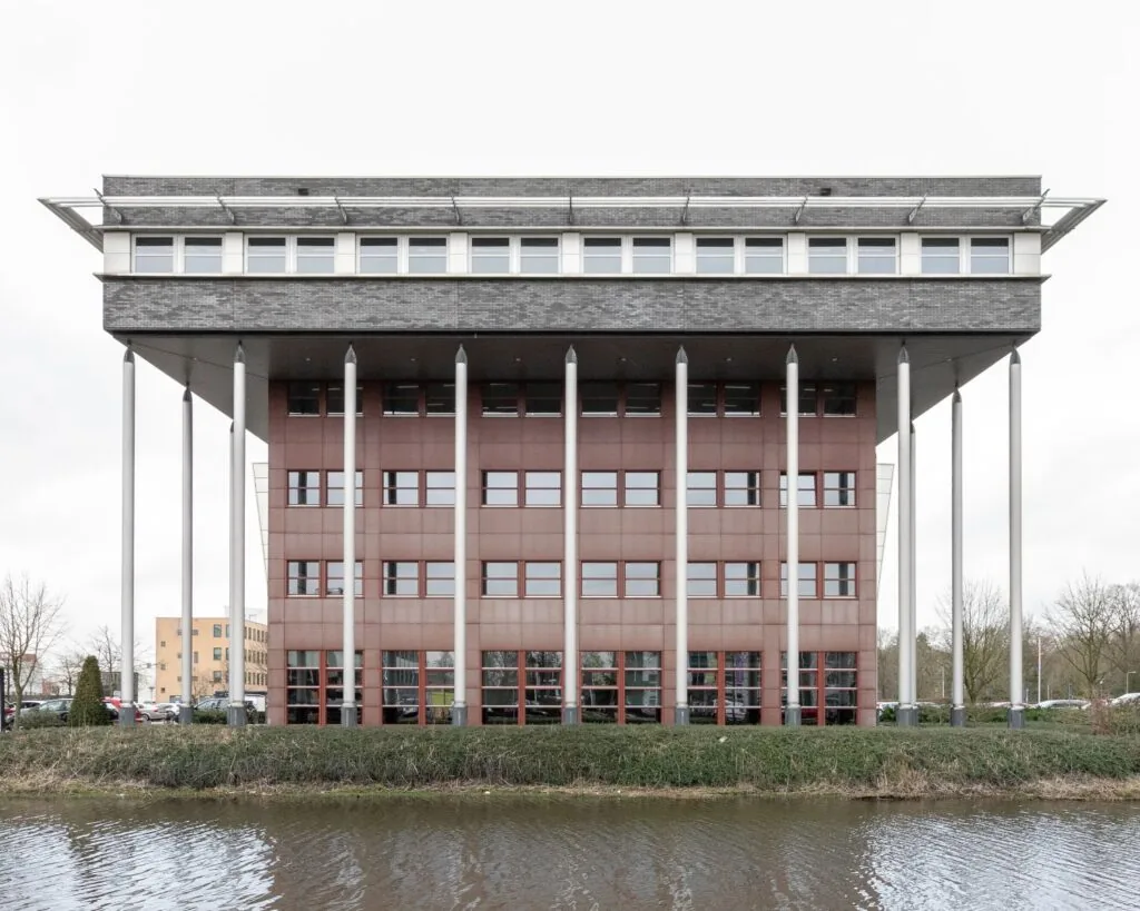 Vooraanzicht van kantoorgebouw Capitool 10 in Enschede, met opvallende kolommen en waterpartij op de voorgrond.