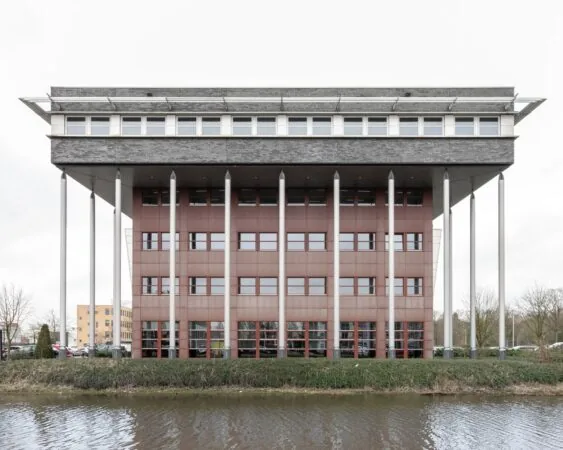 Vooraanzicht van kantoorgebouw Capitool 10 in Enschede, met opvallende kolommen en waterpartij op de voorgrond.