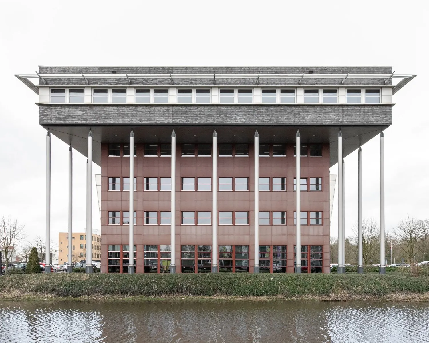 Vooraanzicht van kantoorgebouw Capitool 10 in Enschede, met opvallende kolommen en waterpartij op de voorgrond.