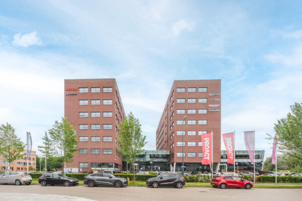 Twee bakstenen kantoorgebouwen met diverse bedrijfslogo's, waaronder Xerox en Proact, aan de Rijnzathe met auto's geparkeerd op de voorgrond.