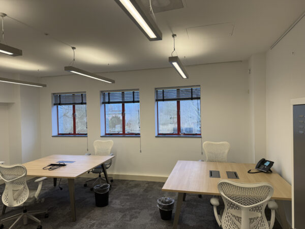 Modern kantoorruimte 1.01D met bureaus, ergonomische stoelen, telefoontoestel en drie ramen met jaloezieën.