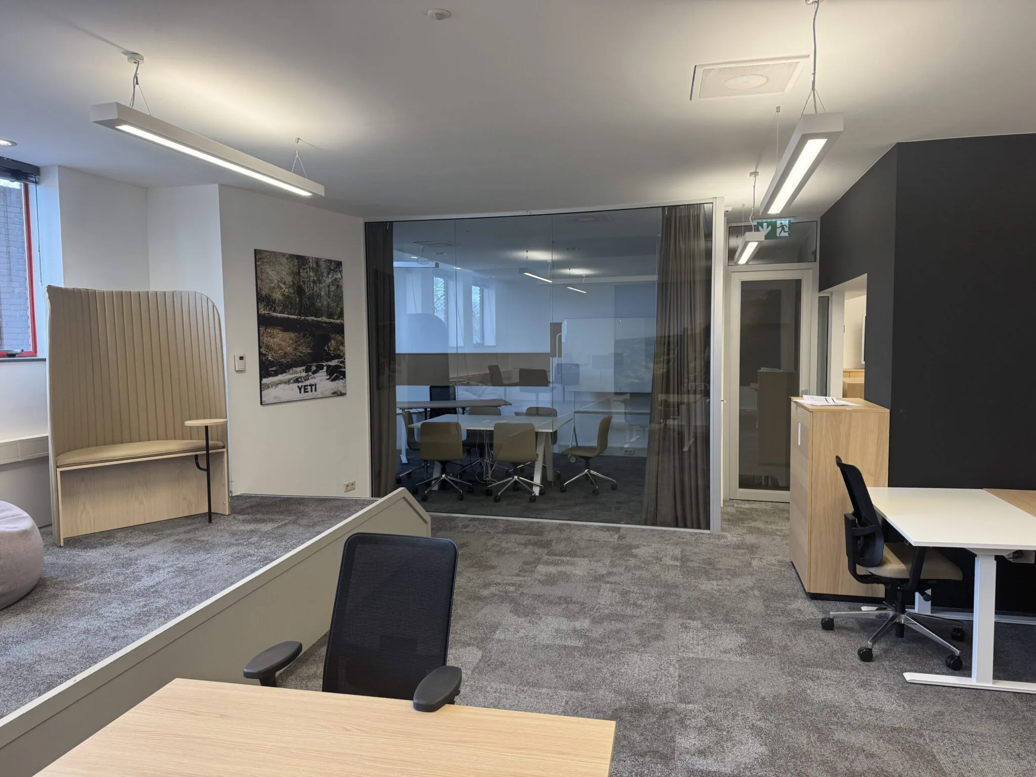 Moderne kantoorruimte met glazen vergaderruimte, open werkplekken en een zitnis met hoge rugleuning.