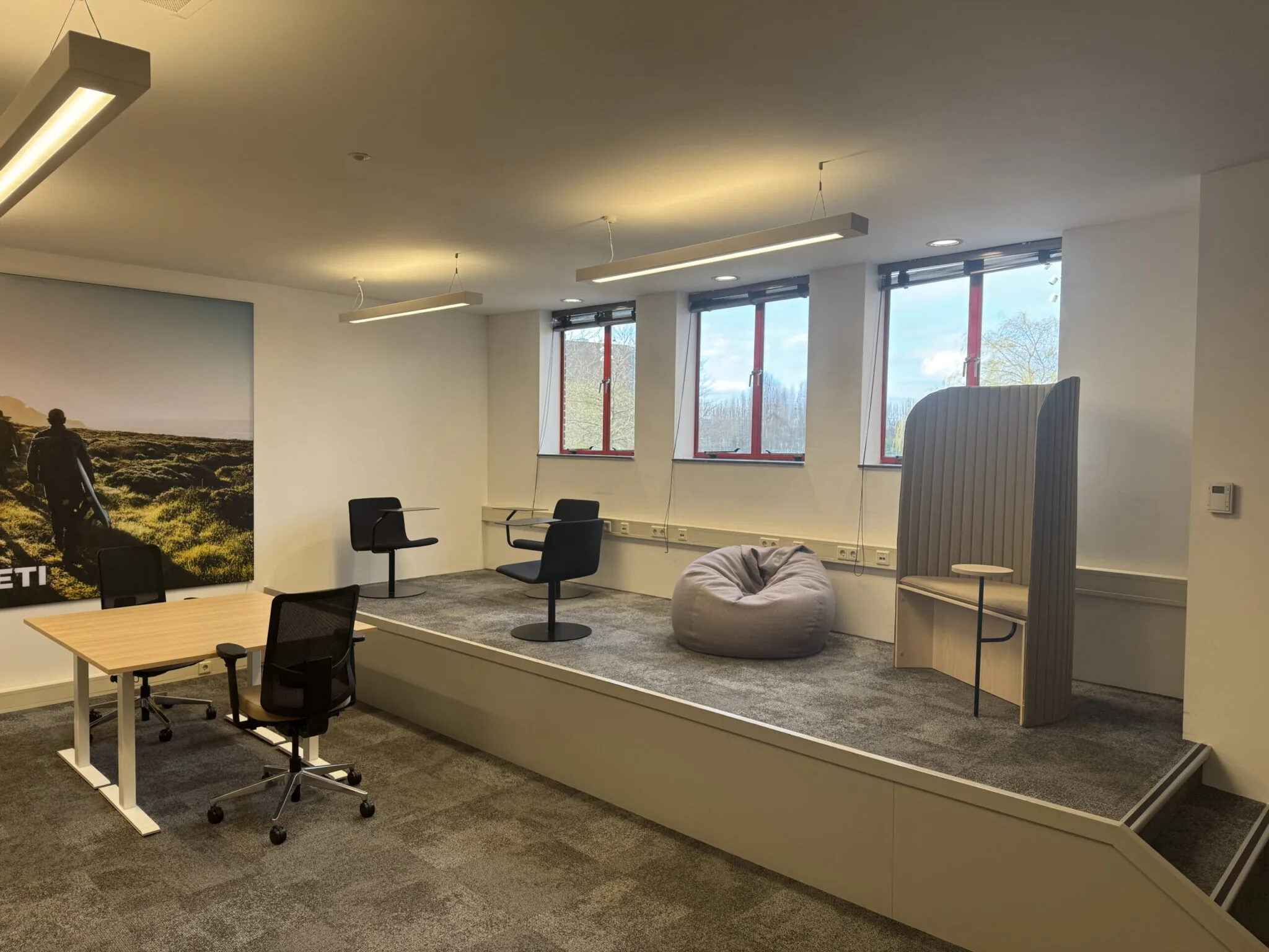 Modern kantoor met verhoogd zitgedeelte, inclusief loungezitjes, een zitzak, bureaustoelen en grote ramen.