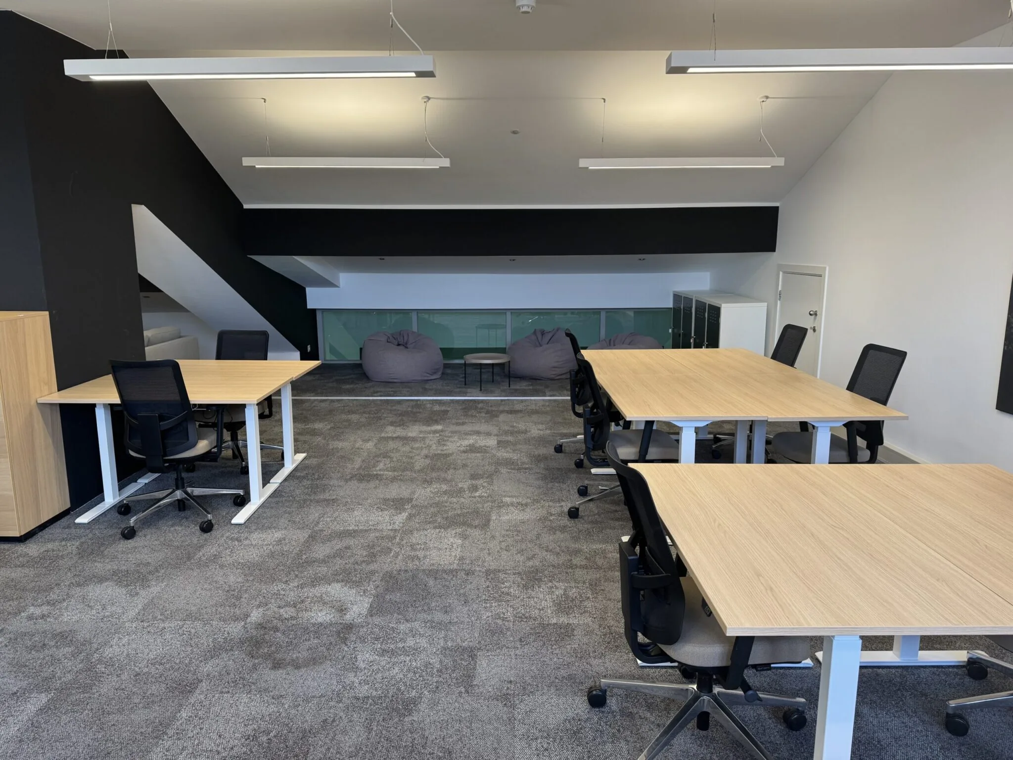Moderne kantoorruimte met meerdere bureaus, bureaustoelen en zitzakken in de achtergrond.