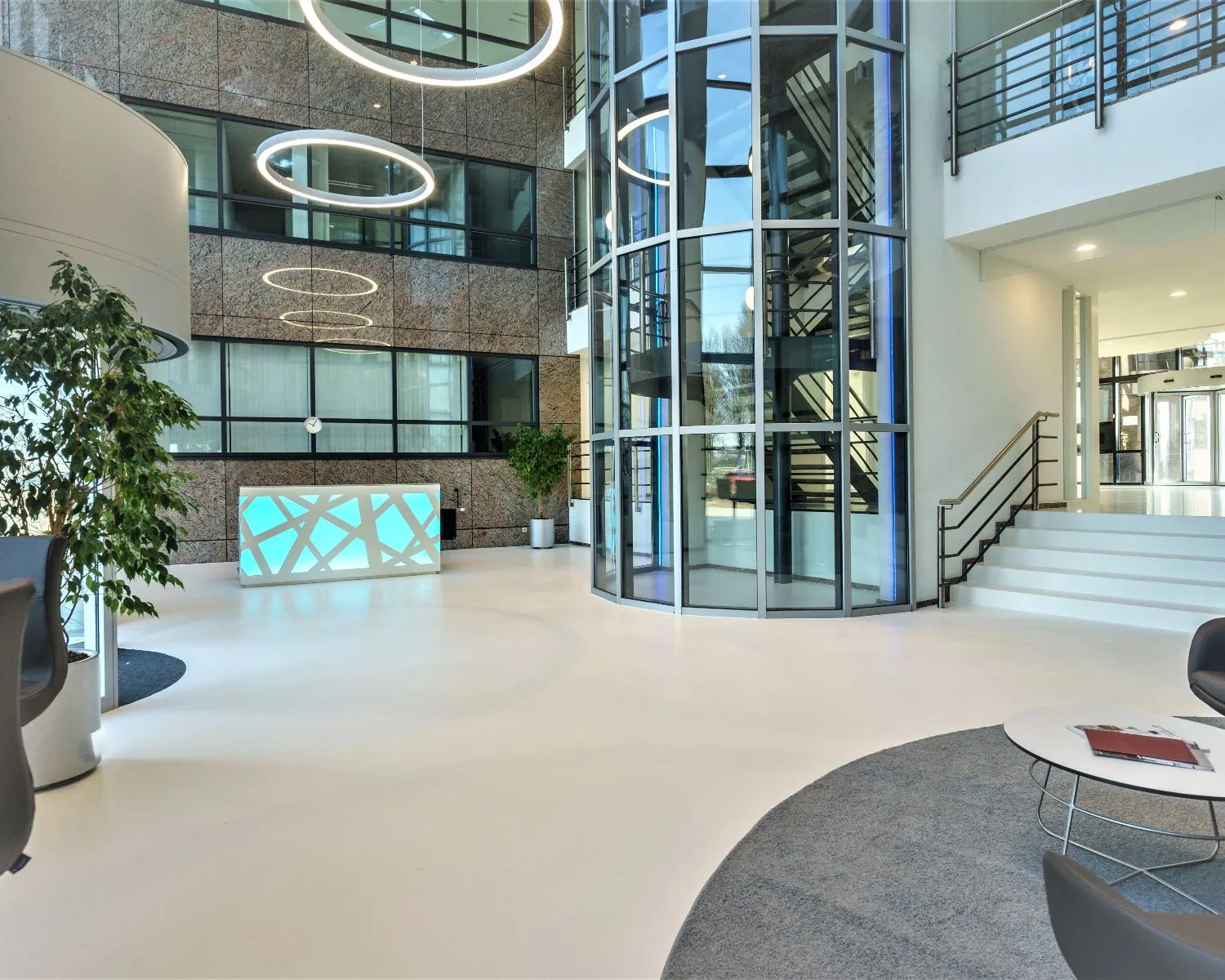 Moderne en lichte entreehal met een receptiebalie, glazen lift en stijlvolle verlichting.