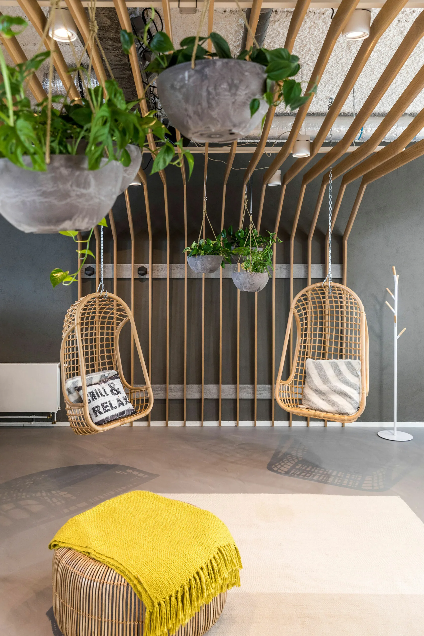 Loungehoek in HNK Rotterdam Centrum met hangstoelen, planten en een rotan poef met gele plaid.