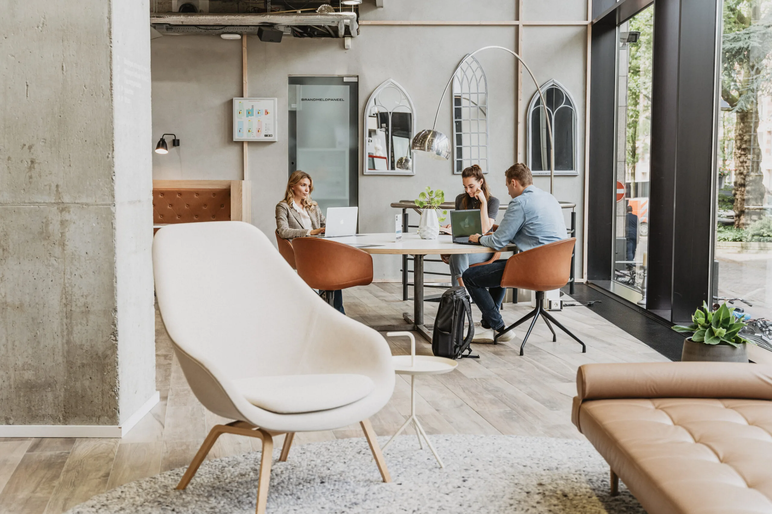 Drie mensen werken op laptops aan een ronde tafel in een moderne, lichte werkruimte bij HNK Utrecht CS.
