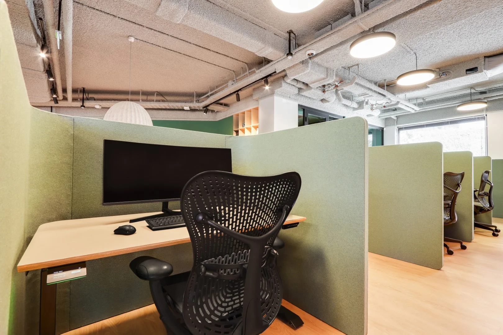 Flexwerkplek met bureaustoel, computerscherm en groene scheidingswanden in Sloterdijk coworkingruimte.