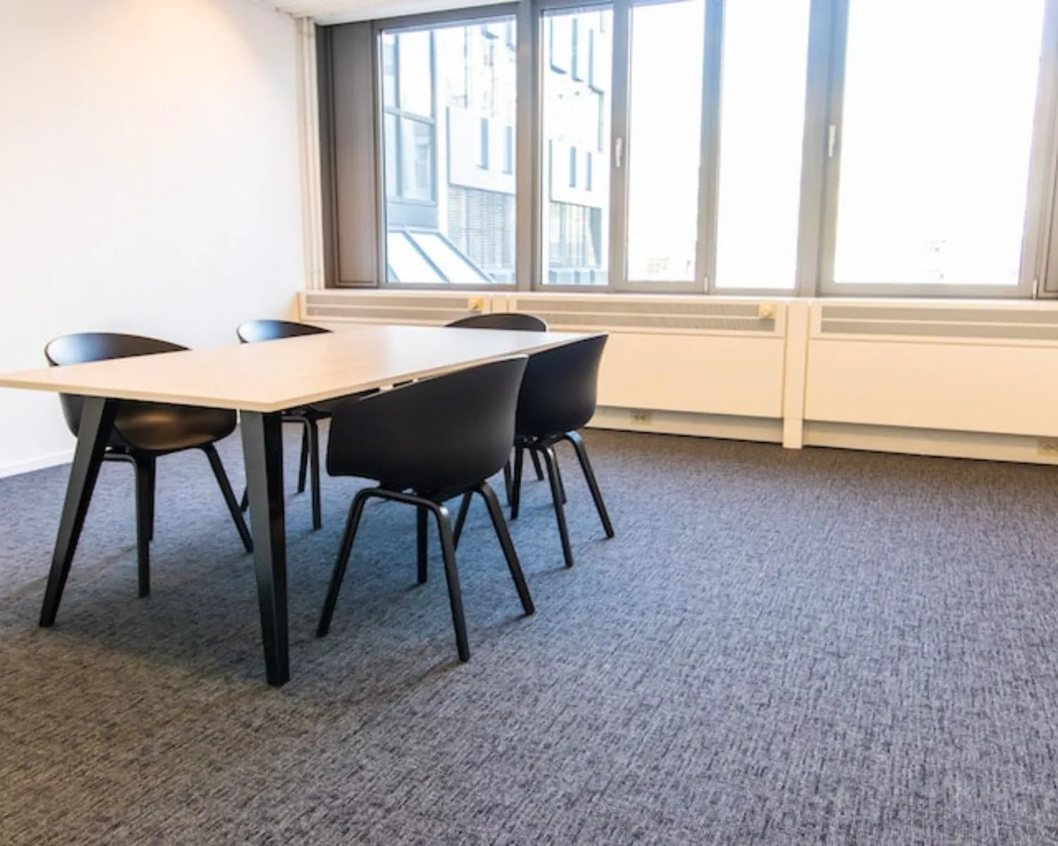 Moderne kantoorkamer met grote ramen, een tafel en vier zwarte stoelen aan de Gaetano Martinolaan 75-95 in Maastricht.