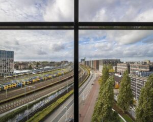 Uitzicht vanuit kantoorruimte aan het Rietlandpark in Amsterdam op spoorlijnen, treinen, wegverkeer en omliggende gebouwen.