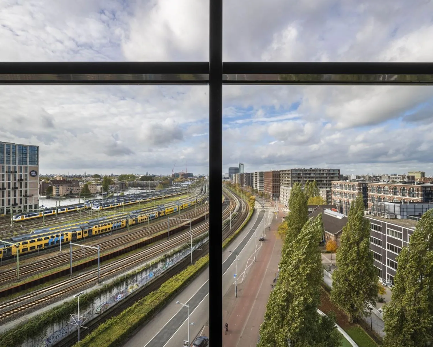 Uitzicht vanuit kantoorruimte aan het Rietlandpark in Amsterdam op spoorlijnen, treinen, wegverkeer en omliggende gebouwen.