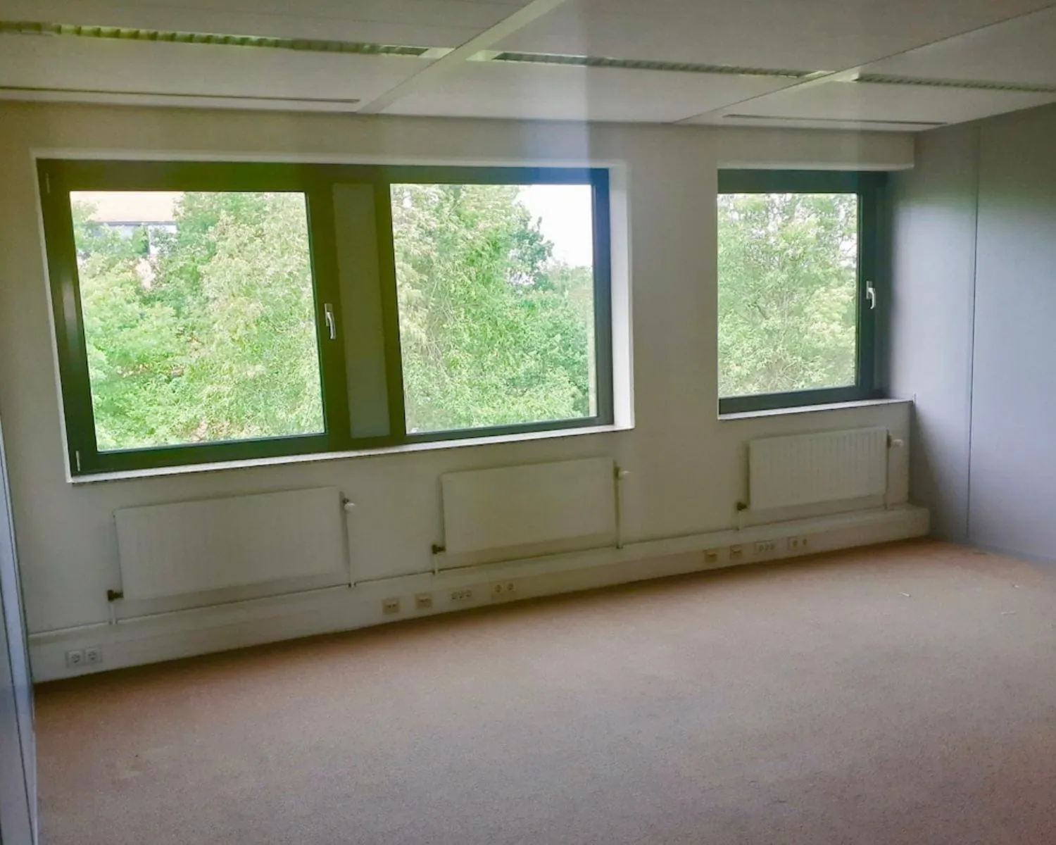 Lege kantoorruimte met drie grote ramen aan de Hardwareweg in Amersfoort, met uitzicht op groen.
