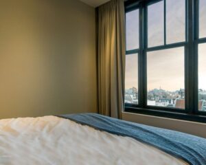 Slaapkamer met groot raam en uitzicht op de Amsterdamse binnenstad vanuit kantoorruimte aan de Westermarkt 2.