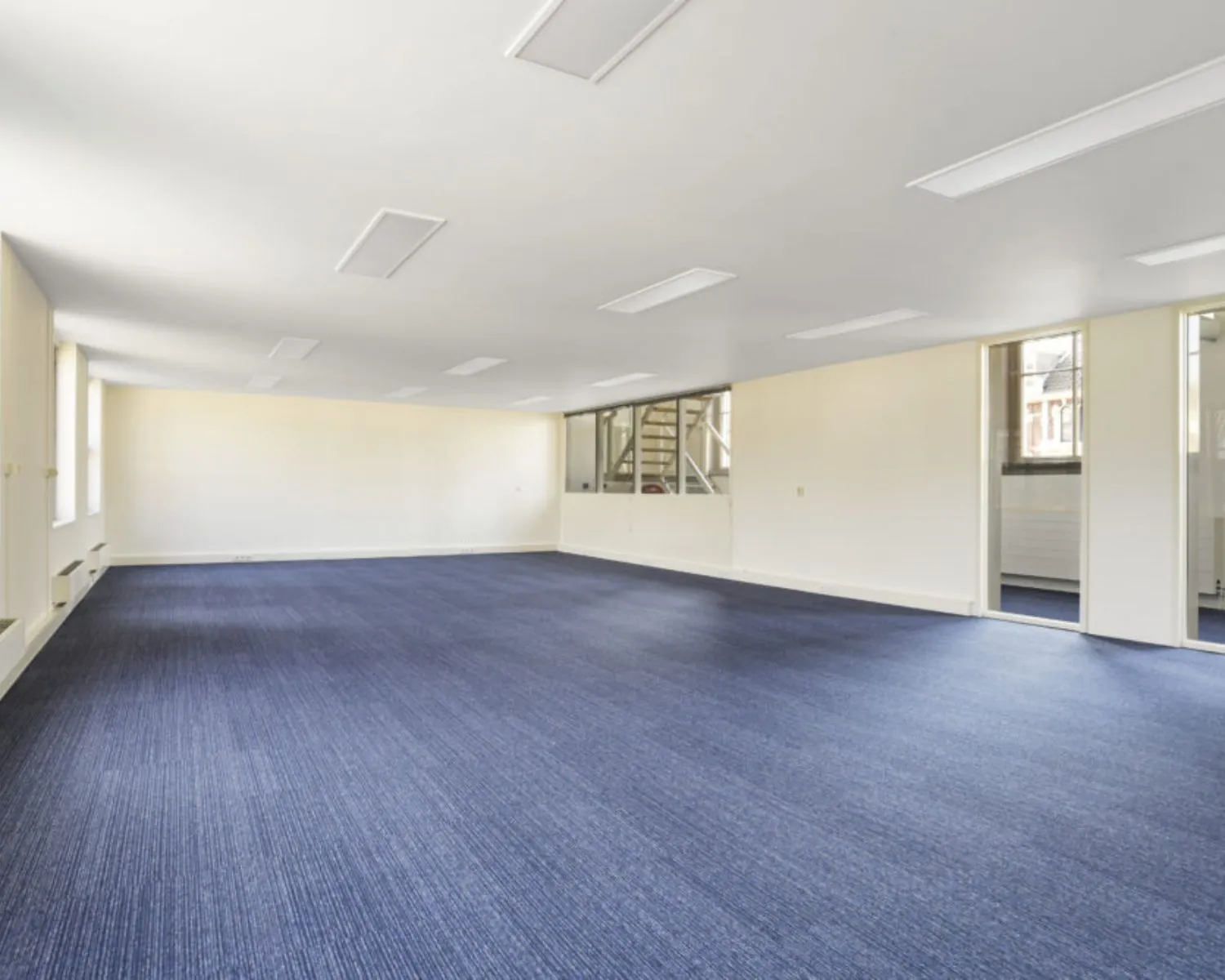 Lichte, ruime kantoorruimte met blauw tapijt aan de Wilhelminastraat 43a in Haarlem.