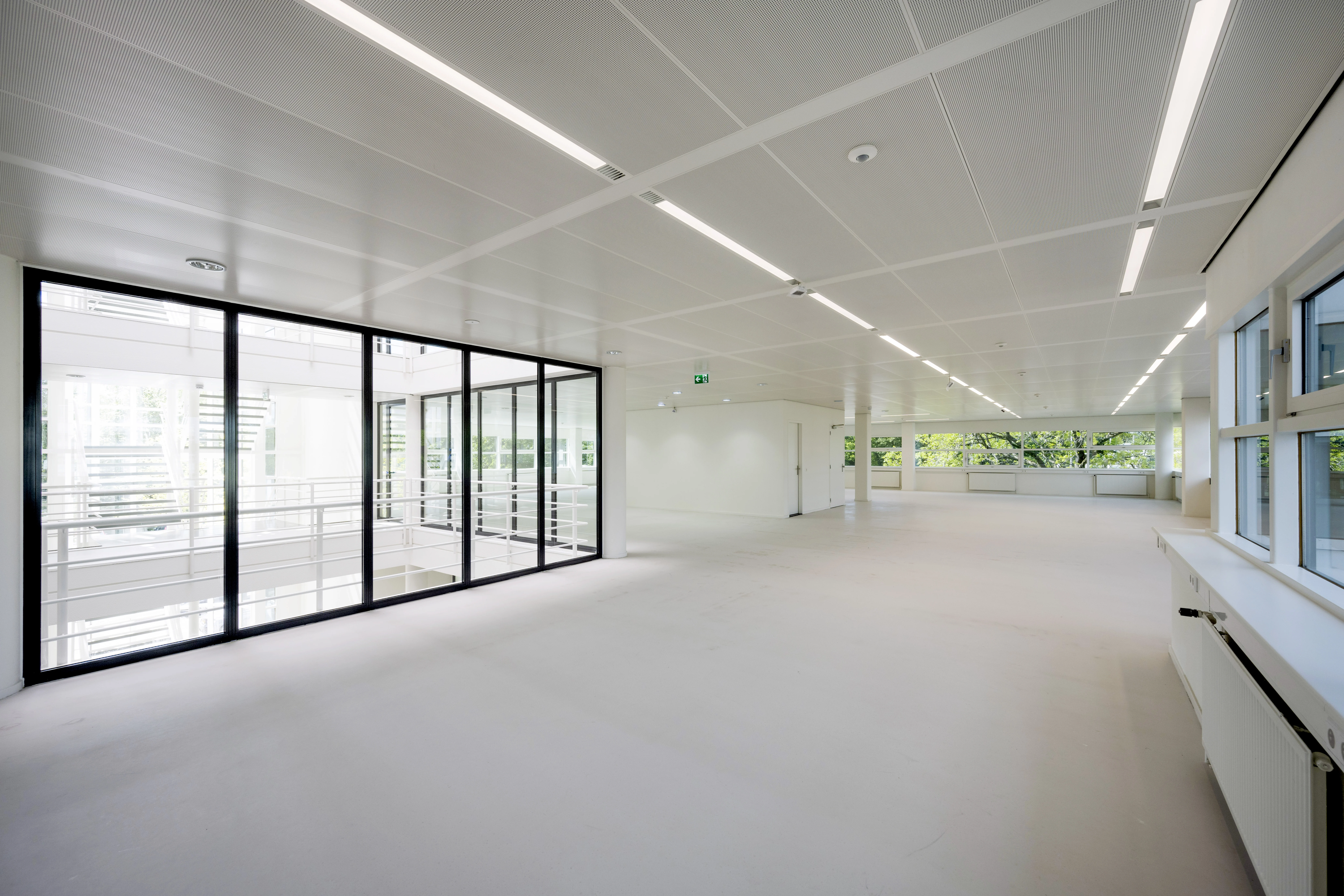 Lichte, lege kantoorruimte in gebouw Zuidoost 052 met grote ramen en glazen wand.