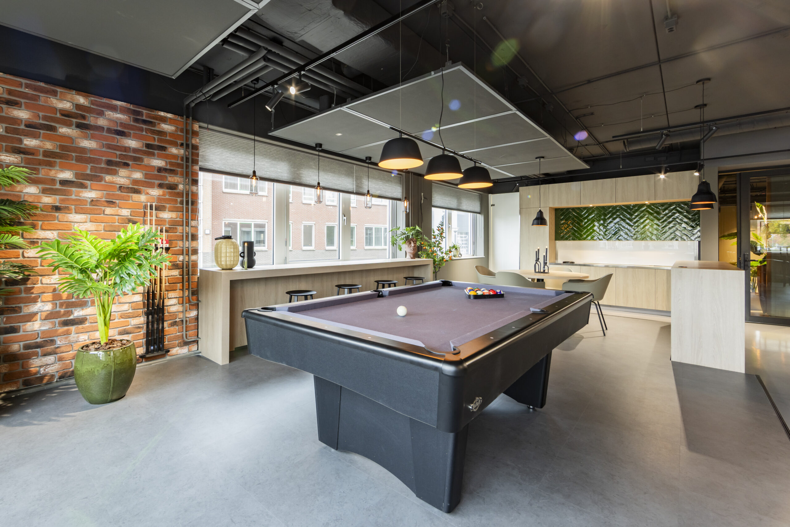 Een moderne recreatieruimte met een biljarttafel, bakstenen muur en planten.