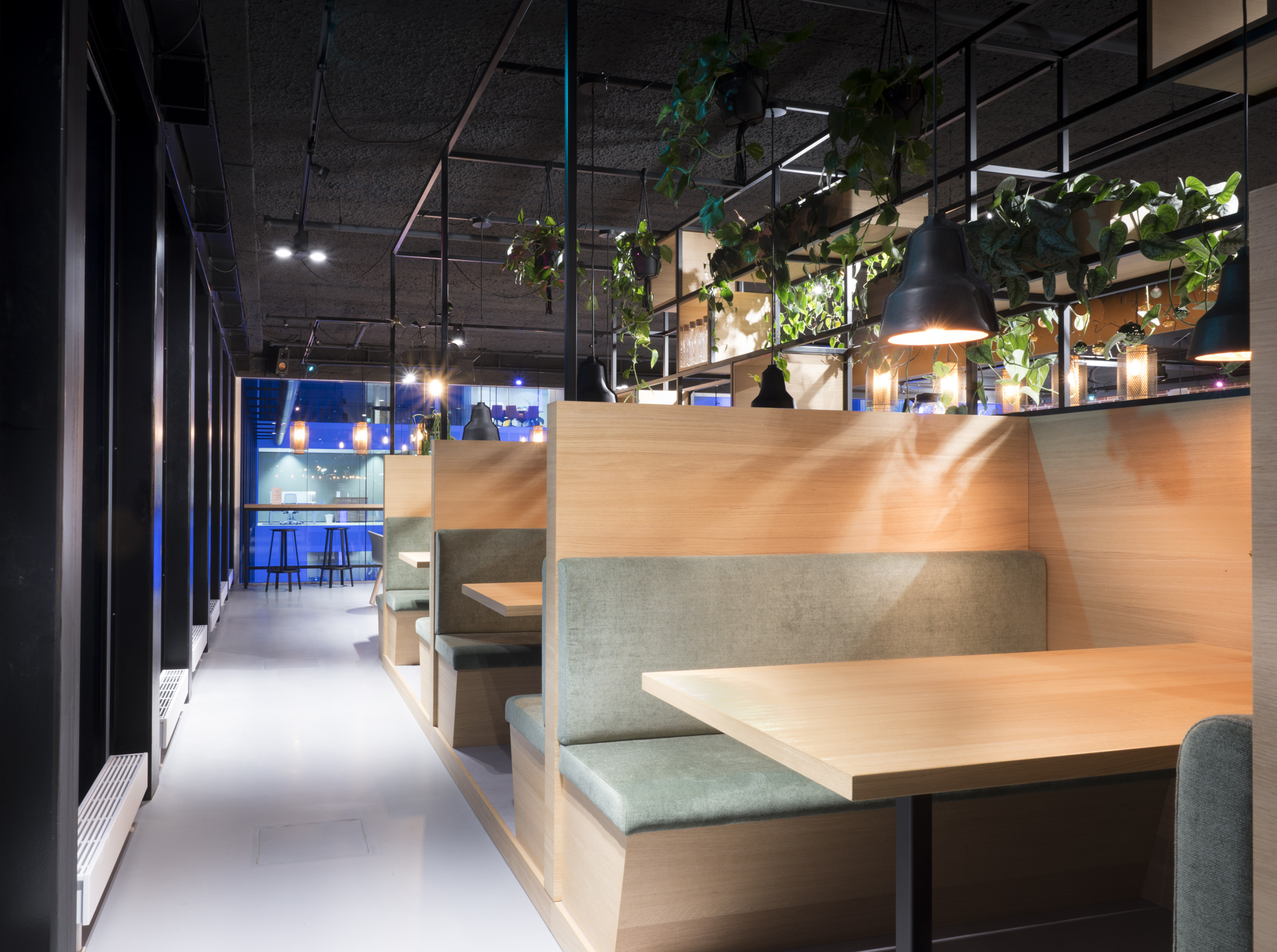 Moderne zitplaatsen in treinstijl met gezellige verlichting en groene planten in een clubachtige omgeving.