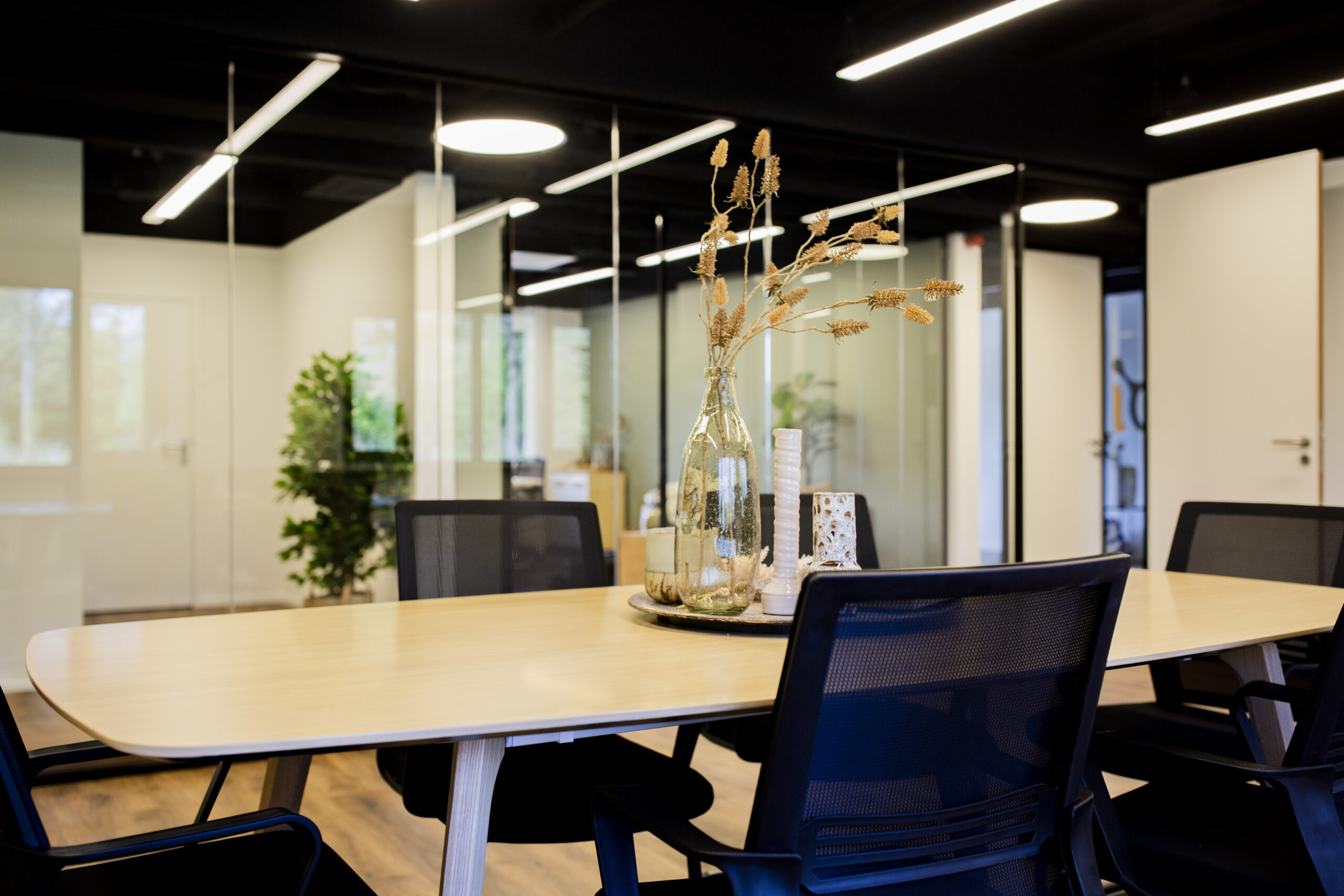 Een moderne vergaderruimte in ELE Office Woerden met een houten tafel, zwarte stoelen en een decoratieve glazen fles.