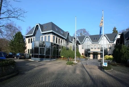 Kantoorgebouw aan de Utrechtseweg met moderne architectuur, vlaggenmast en parkeerterrein op de voorgrond.
