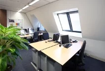 Kantoorruimte aan de Utrechtseweg met bureaus, computers en een schuine wand met raam.