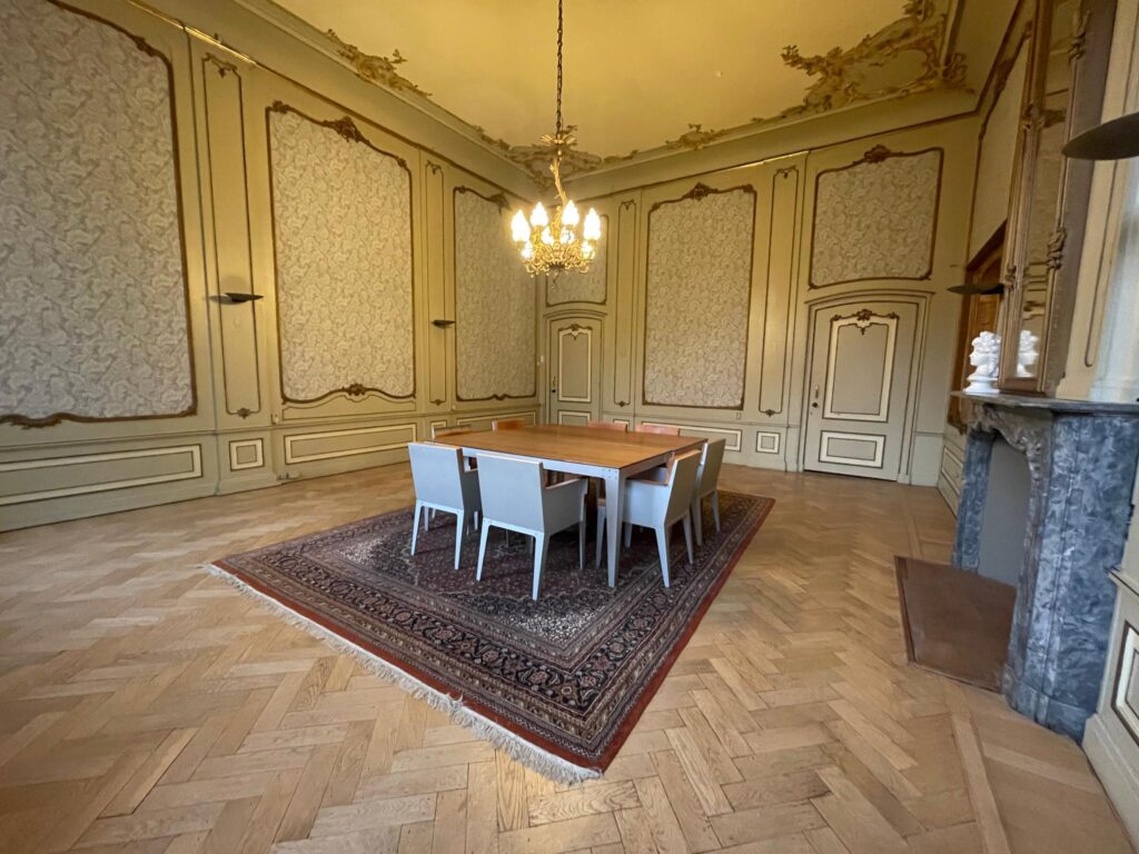 Vergaderruimte aan de Herengracht met klassieke wandpanelen, sierplafond, houten vloer, houten tafel en moderne stoelen op een Perzisch tapijt.