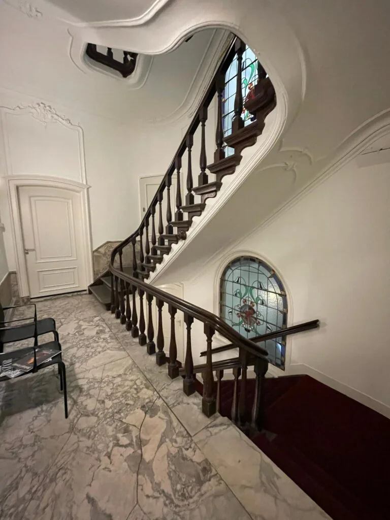 Monumentaal trappenhuis aan de Herengracht met marmeren vloer, houten balustrade en glas-in-loodraam.