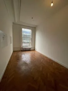 Lichte, lege kamer aan de Herengracht met visgraat houten vloer en groot raam met uitzicht op de straat.