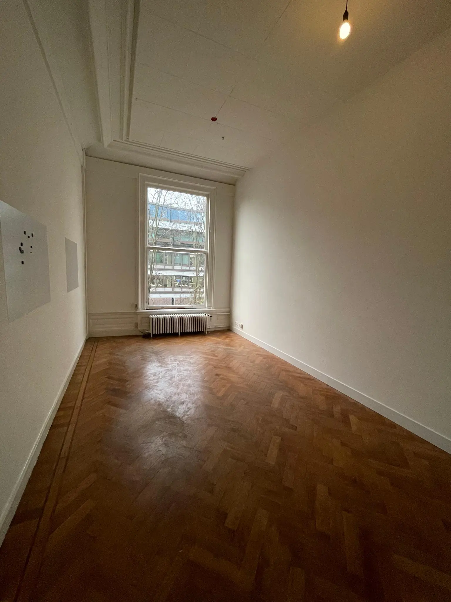 Lichte, lege kamer aan de Herengracht met visgraat houten vloer en groot raam met uitzicht op de straat.