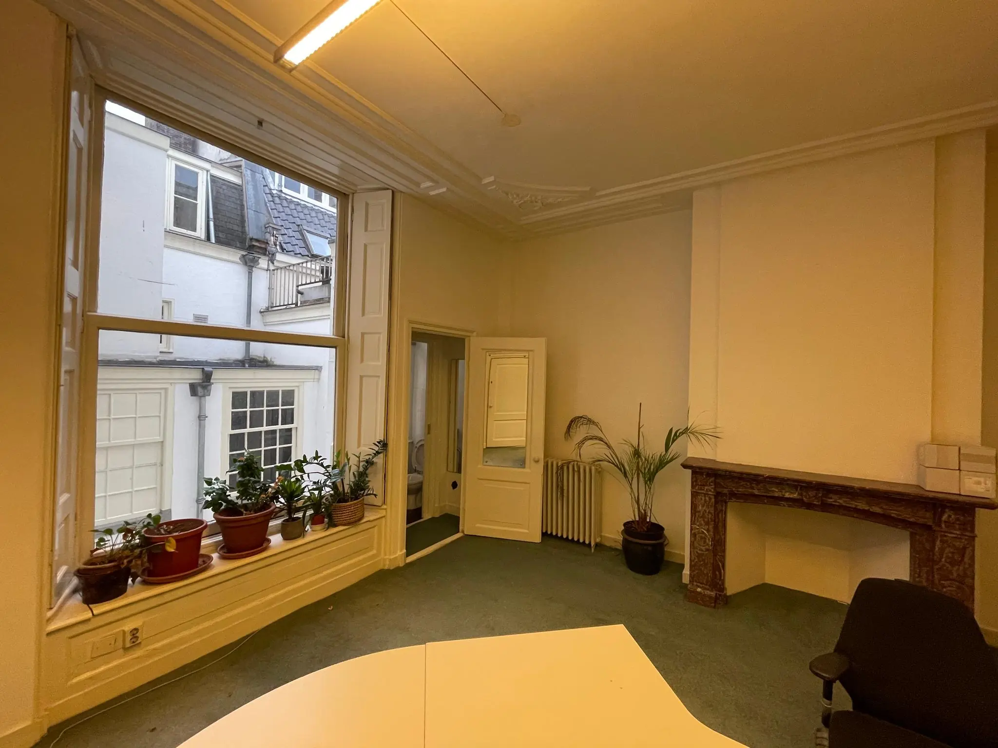 Licht kantoor aan de Herengracht met grote ramen, planten op de vensterbank en een decoratieve schouw.