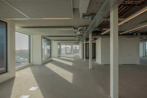 Een open, leeg kantoorruimte met grote ramen, plafonds voorzien van zichtbare ventilatiebuizen.