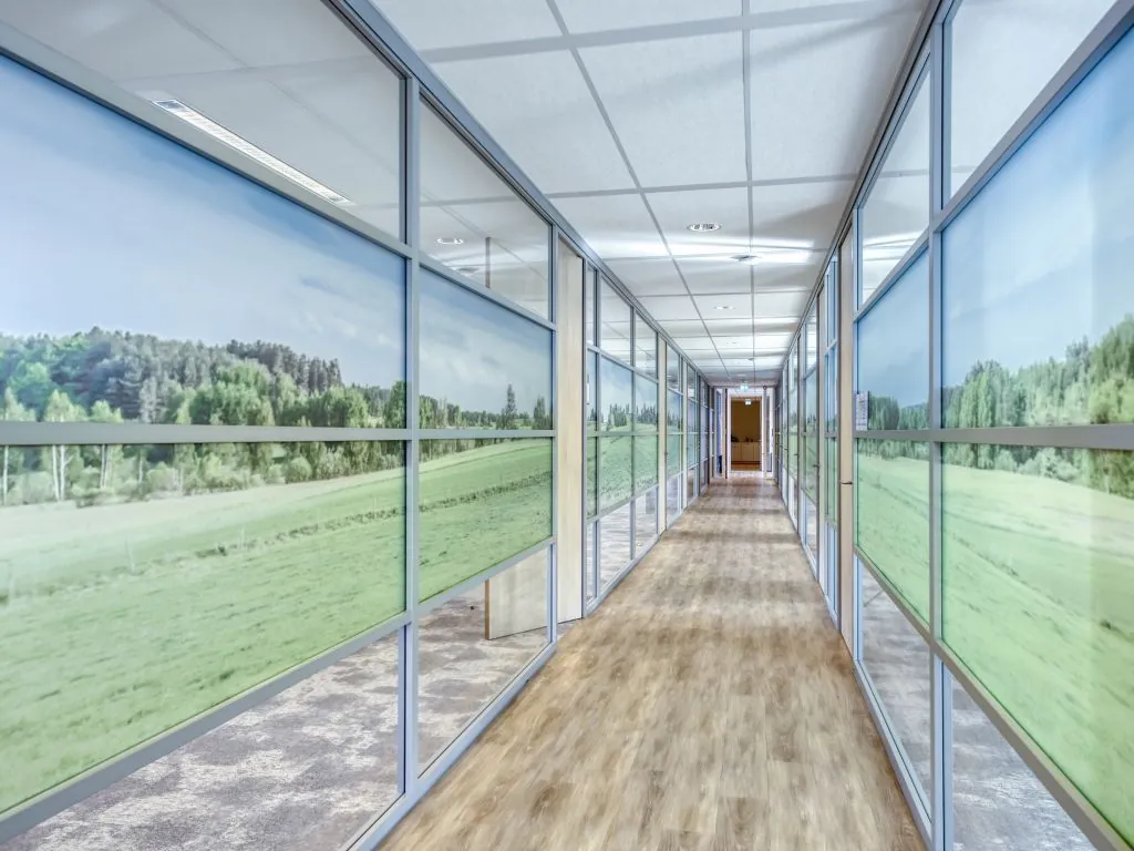 Lange gang in een modern kantoorpand aan de Mercatorlaan met glazen wanden bedrukt met een landschap van weilanden en bomen.