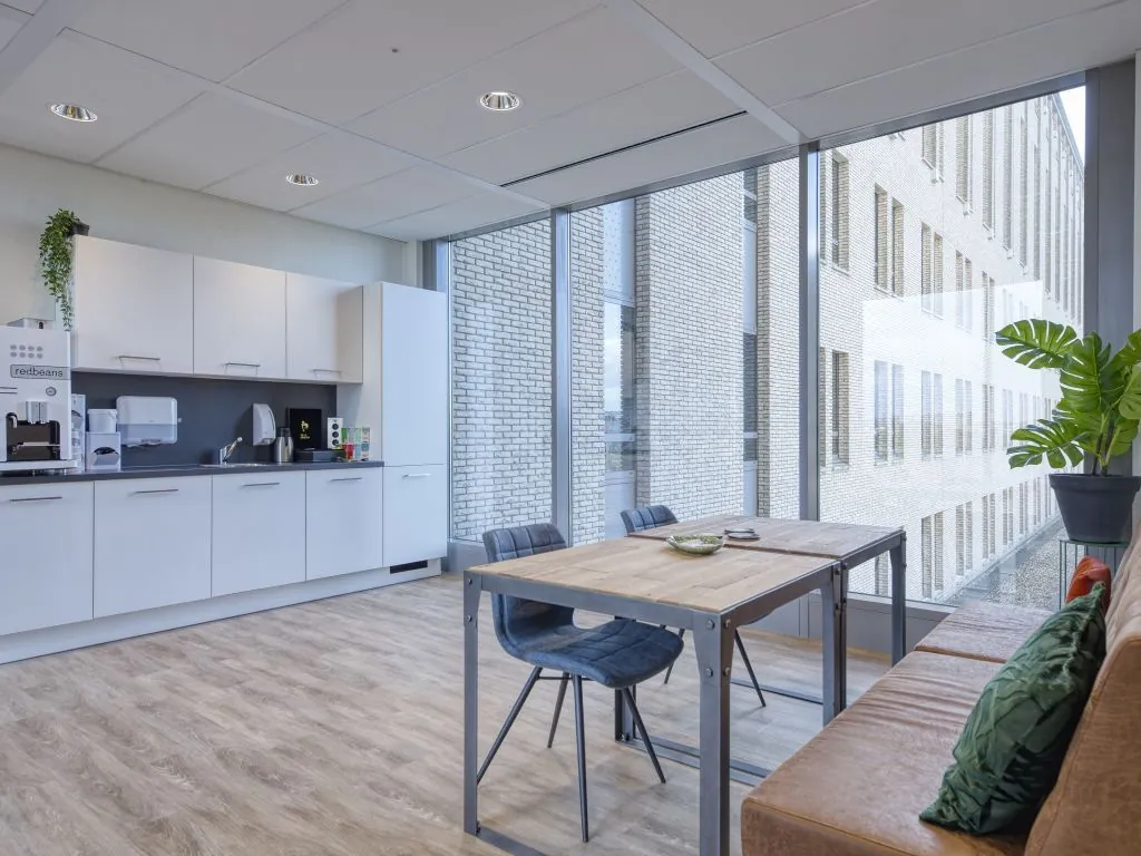Moderne pantry met zithoek in een kantoor aan de Mercatorlaan, met grote ramen en uitzicht op een binnenplaats.