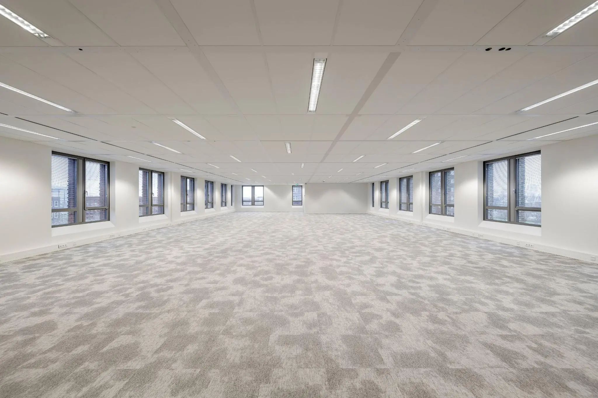 Ruime, leegstaande kantoorruimte aan de Mercatorlaan met grijs tapijt, witte wanden en grote ramen aan beide zijden.