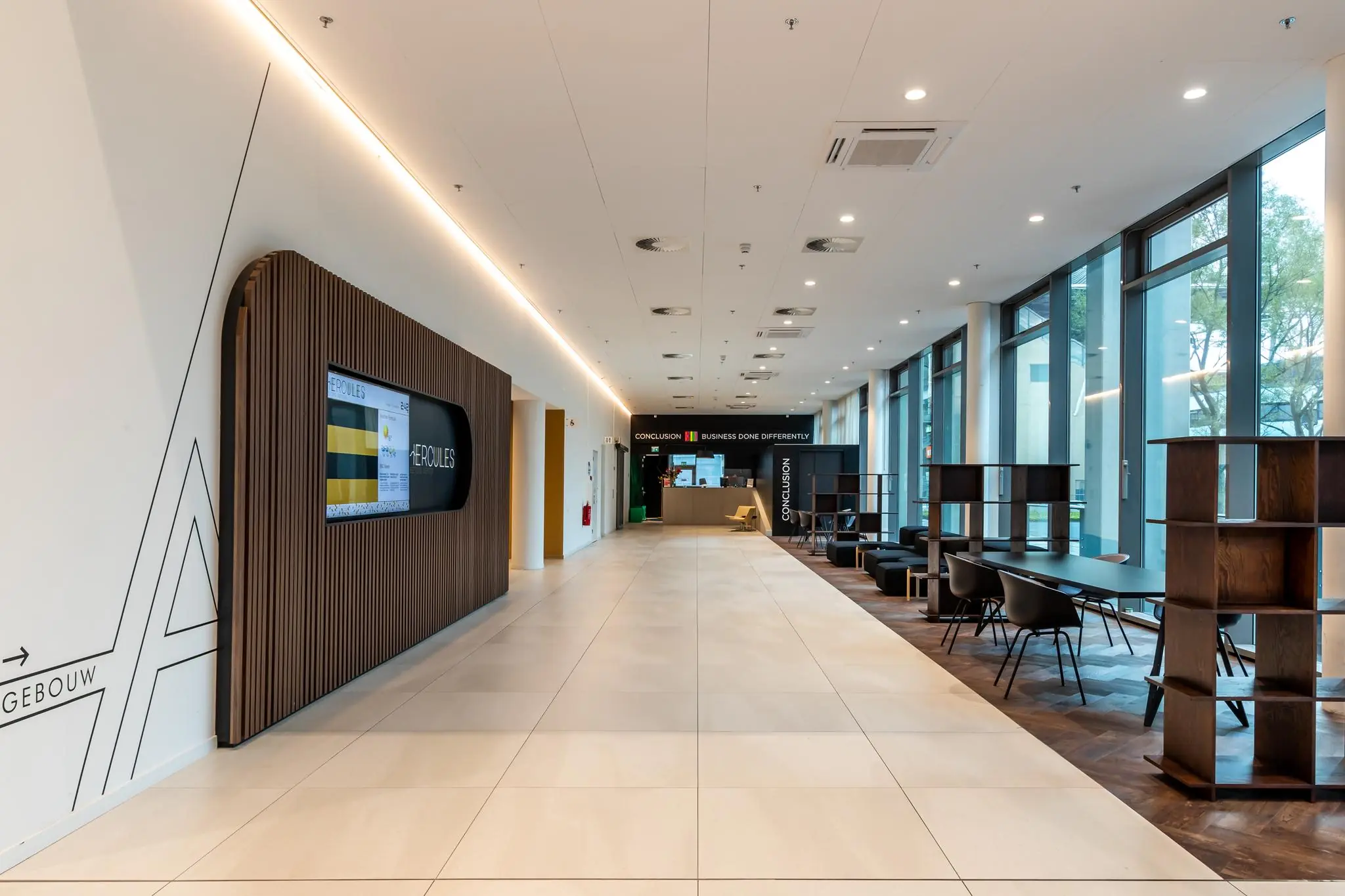 Moderne ontvangsthal van Herculesplein met zithoeken en werkplekken langs grote ramen.