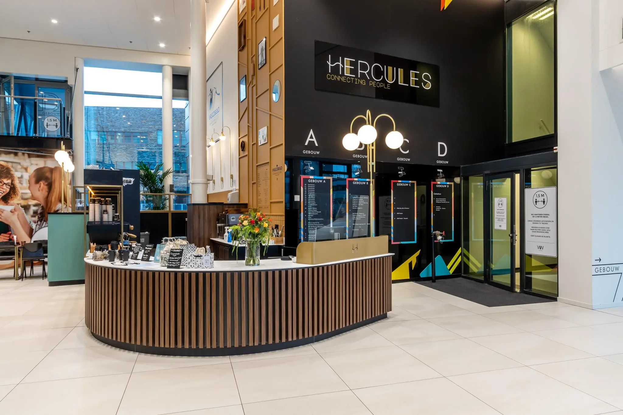 Moderne entreehal van het Herculesplein met balie, bewegwijzering naar gebouwen A t/m D en een koffiestation.