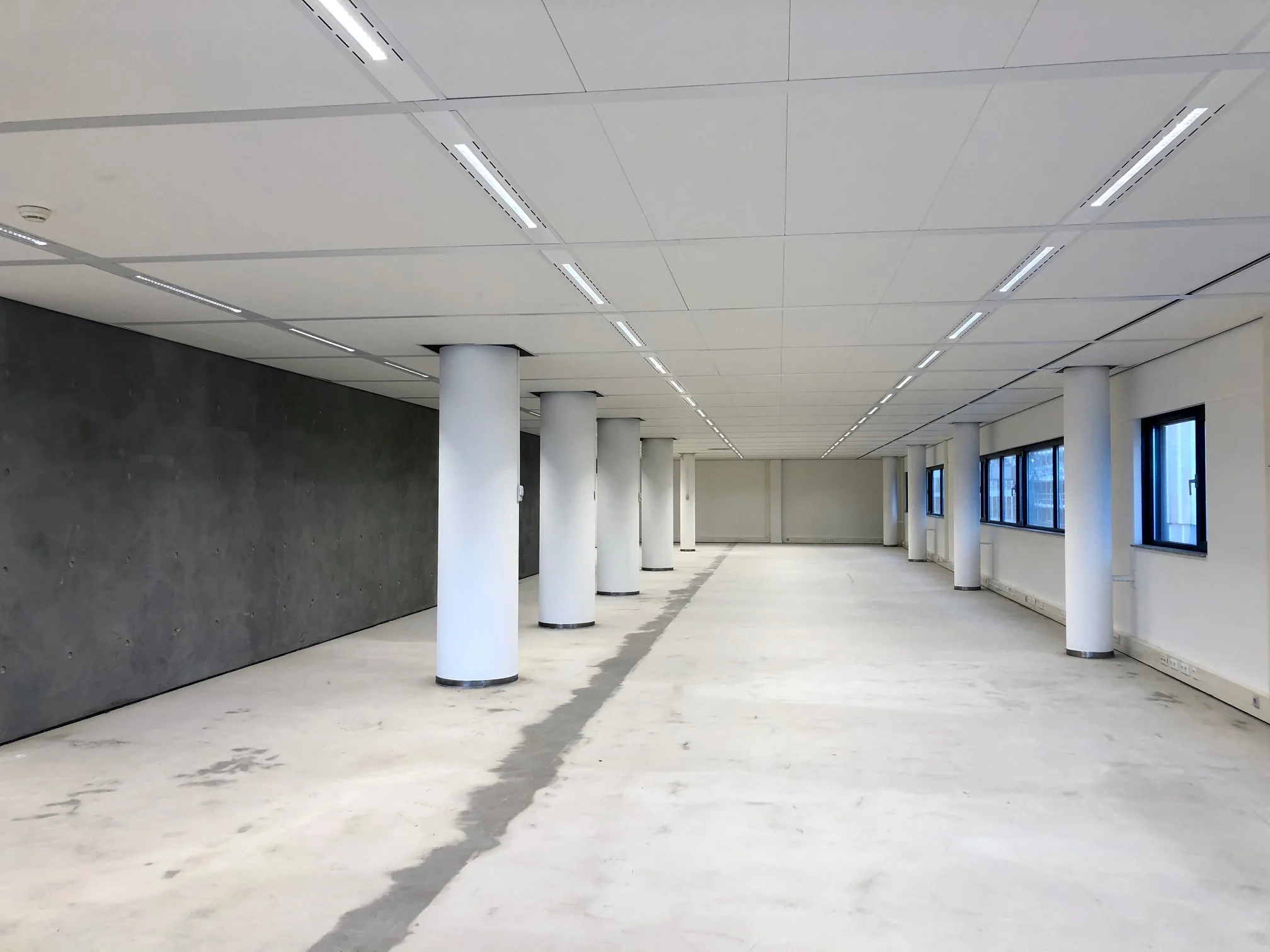 Leeg kantoorpand aan het Willemsplein met witte zuilen, systeemplafond en betonnen vloer.