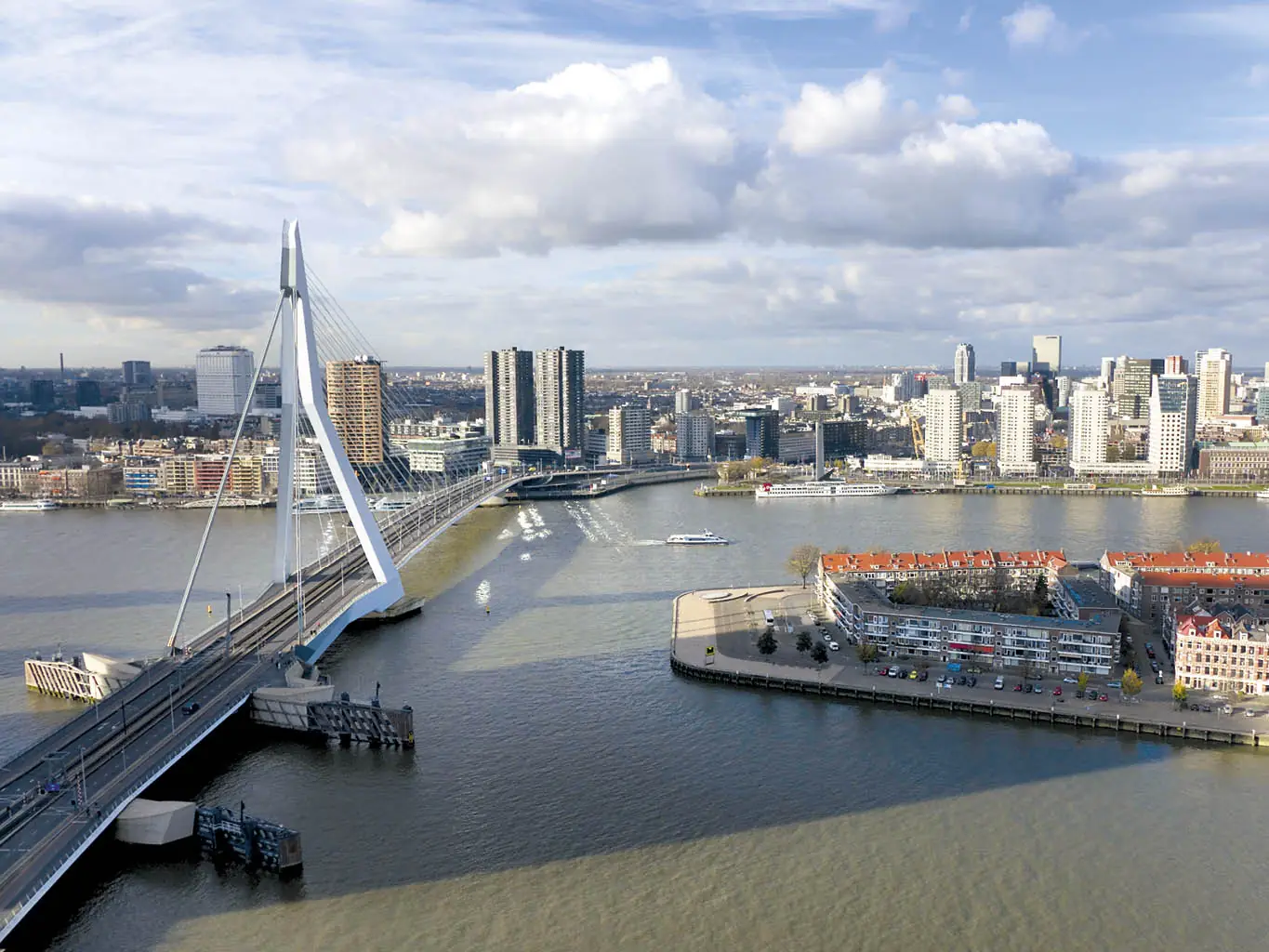 Luchtfoto van de Erasmusbrug over de Maas met het Wilhelminaplein en de skyline van Rotterdam op de achtergrond.