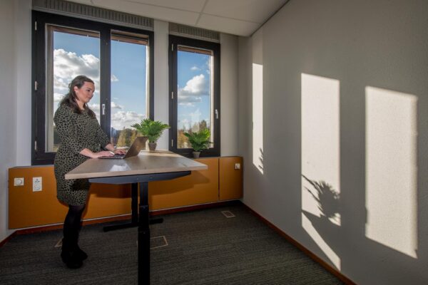 Vrouw werkt op een laptop aan een sta-bureau in een zonovergoten kantoor aan de Fokkerstraat.