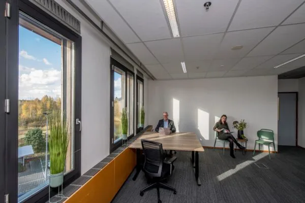 Kantoorruimte aan de Fokkerstraat met twee personen, een man werkend met een laptop aan tafel en een vrouw zittend met een tijdschrift.