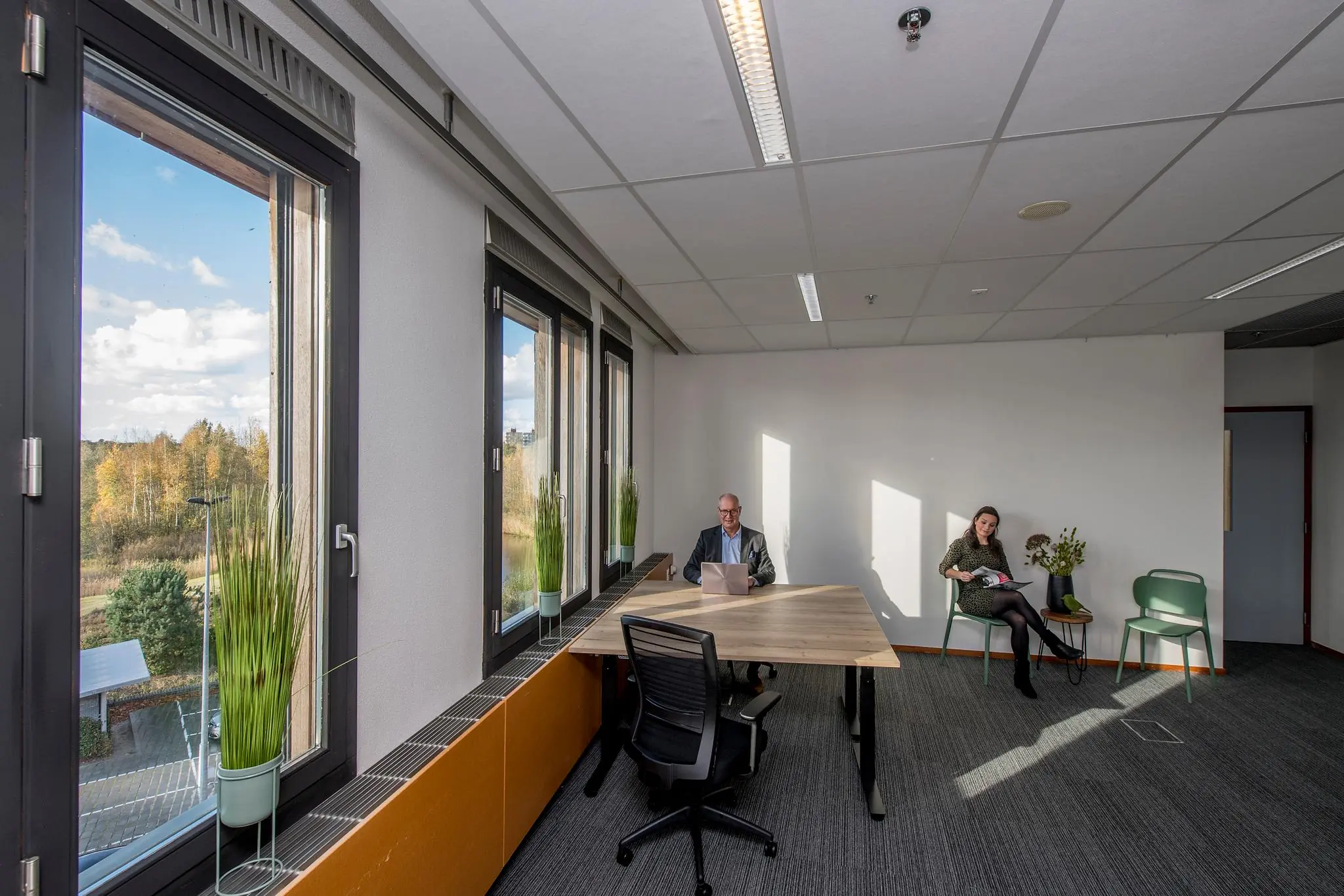 Kantoorruimte aan de Fokkerstraat met twee personen, een man werkend met een laptop aan tafel en een vrouw zittend met een tijdschrift.
