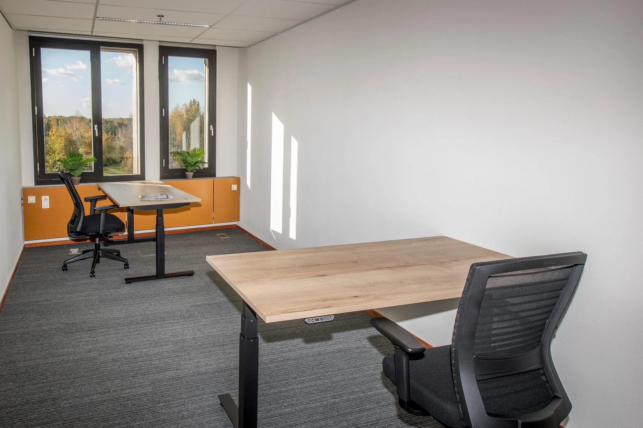Twee moderne bureaus met bureaustoelen in een licht kantoor aan de Fokkerstraat met uitzicht op bomen.