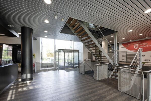 Moderne entreehal van een kantoorpand aan het Rietlandpark met glazen deuren, houten trap en metalen balustrades.