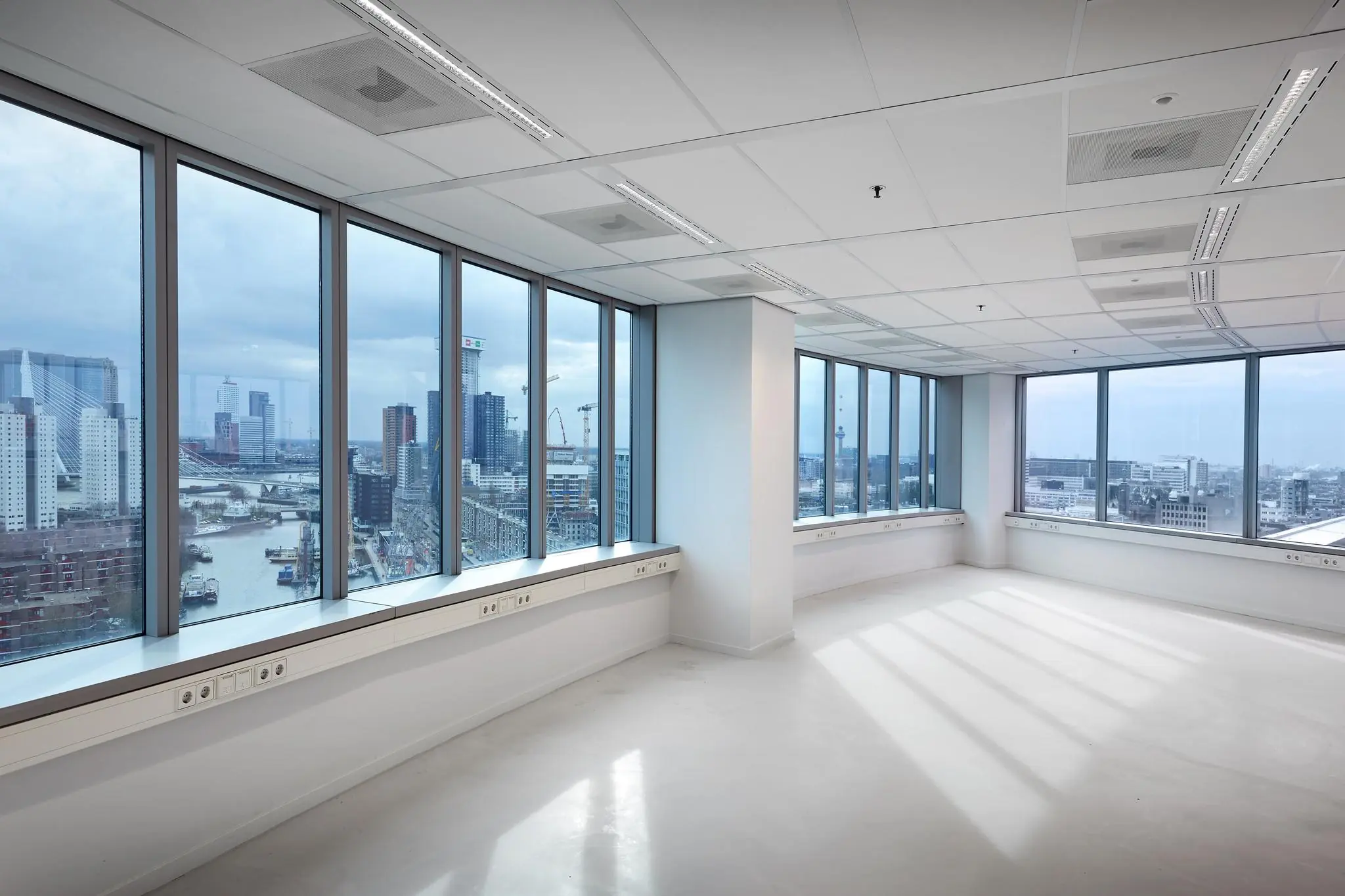 Licht en leeg kantoorpand met panoramisch uitzicht op de skyline van Rotterdam, inclusief de Blaak en Erasmusbrug.