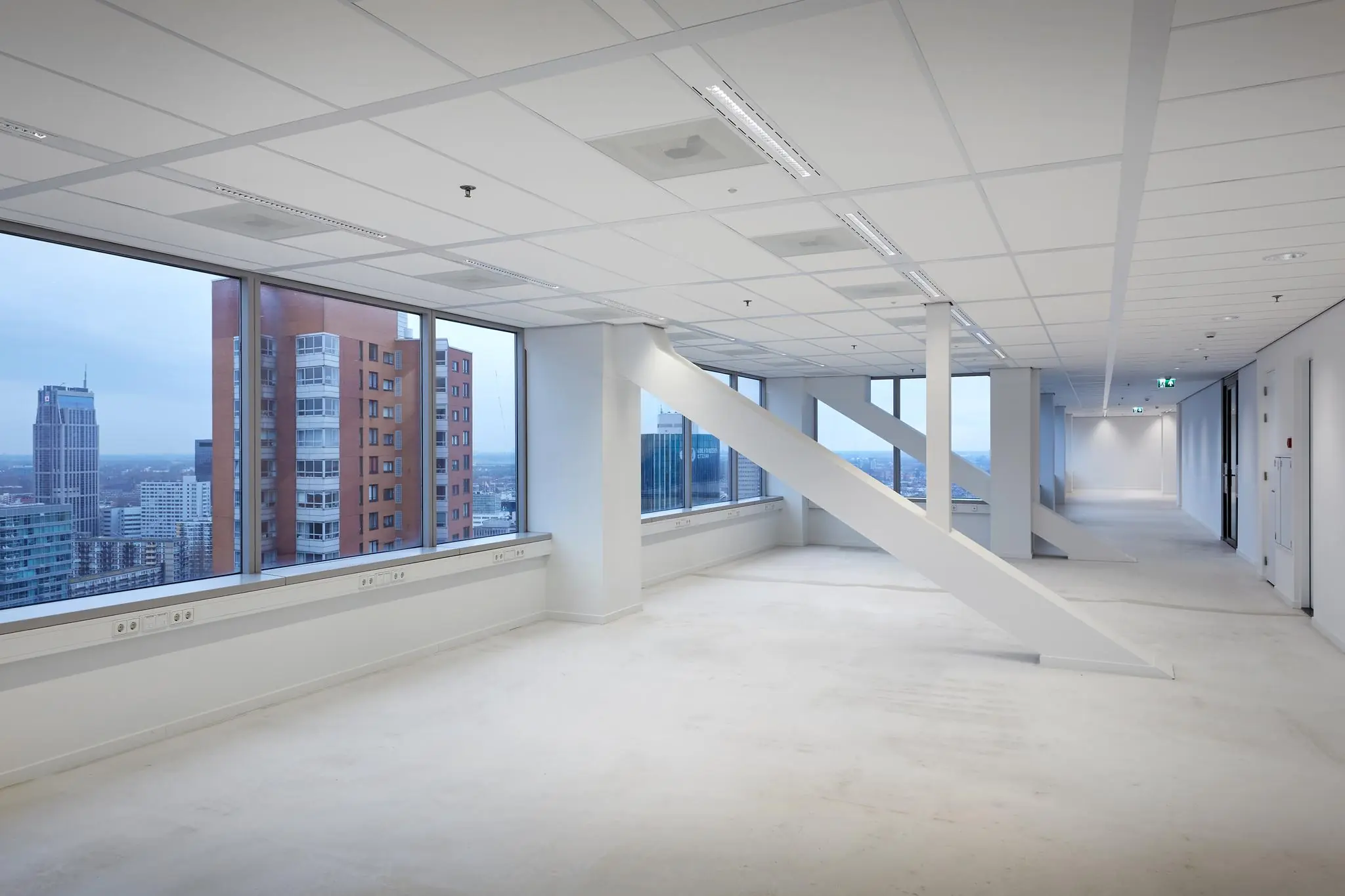 Lichte, lege kantoorruimte in gebouw Blaak met grote ramen en uitzicht op de skyline van Rotterdam.