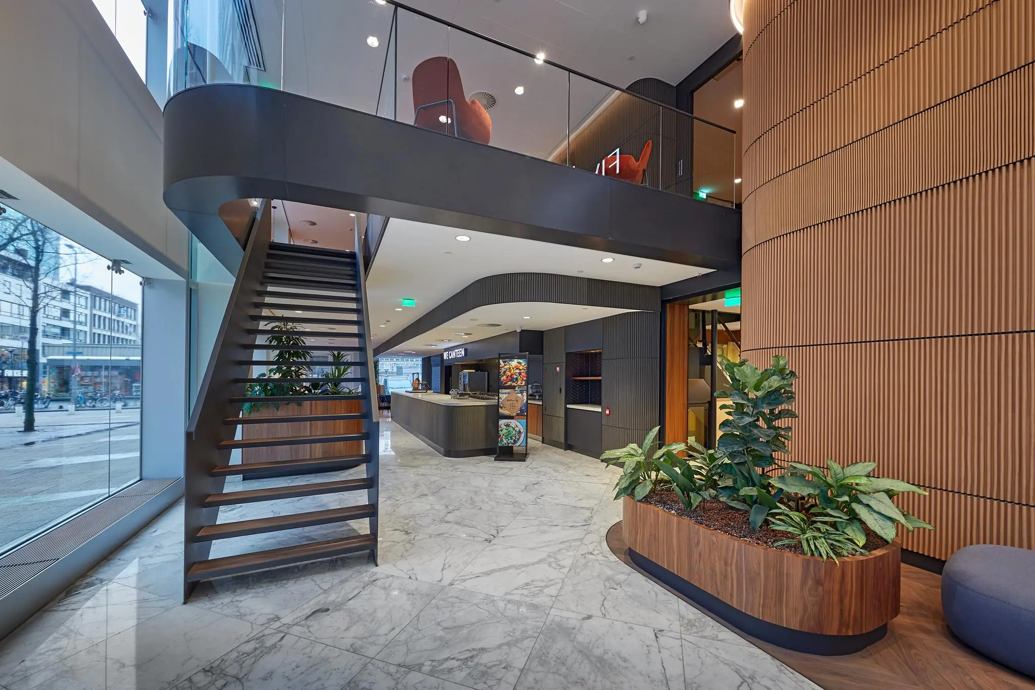 Moderne hotel- of kantoorlobby aan de Blaak met marmeren vloer, plantenbakken, zitgedeelte en zwevende trap naar de bovenverdieping.