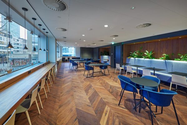 Moderne kantoorlounge in gebouw Blaak met houten visgraatvloer, kleurrijke zitplekken en uitzicht op de stad.