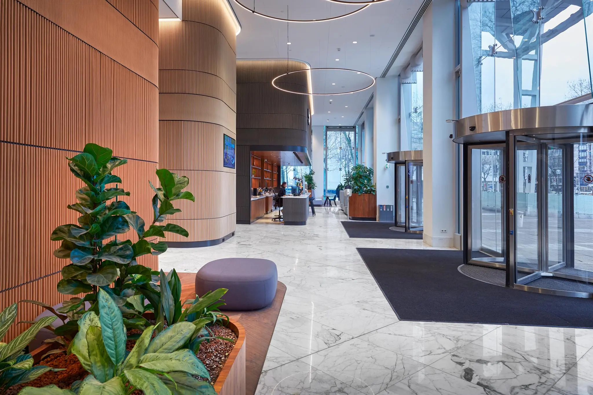 Moderne ontvangsthal van Blaak 16 in Rotterdam met marmeren vloer, houten wanden, planten en een receptiebalie.