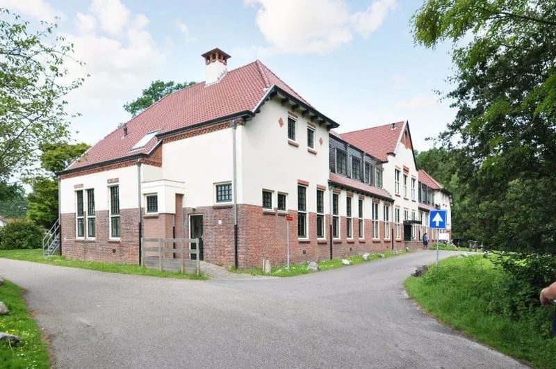 Wit met rood bakstenen gebouw aan de Spechtlaan op een bochtige weg in een groene omgeving.