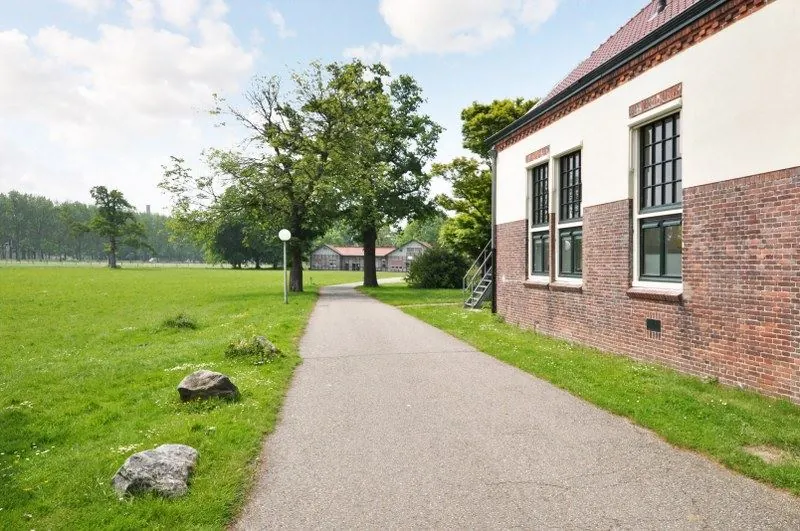 Bakstenen gebouw aan de Spechtlaan met een fietspad en grasveld onder een blauwe lucht.