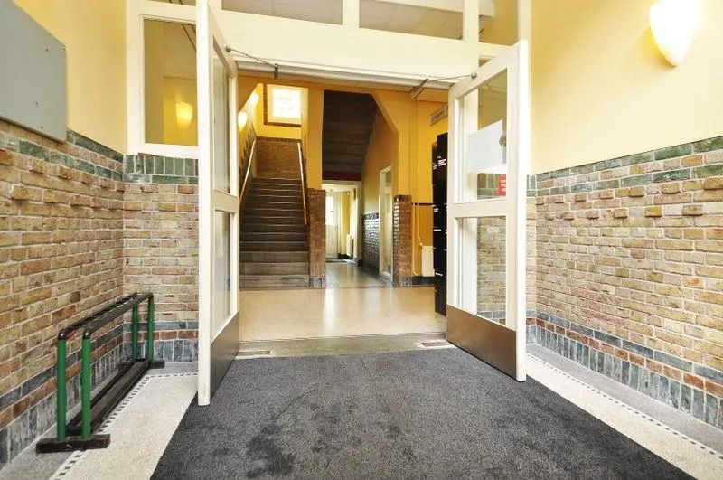 Ingang van een trappenhuis in een jaren ’30 stijl appartementencomplex aan de Spechtlaan, met openstaande deuren en gemetselde muren.